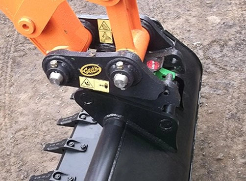 Top view of Geith Manual QR Quick Coupler on machinery, showcasing safety labels and robust black connectors with orange equipment arms.