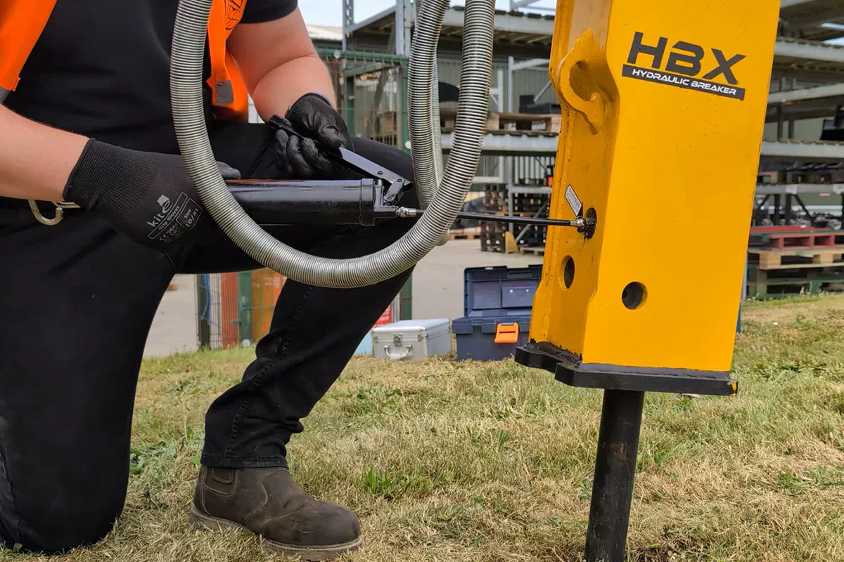 Technician greasing a hydraulic breaker attachment during routine maintenance