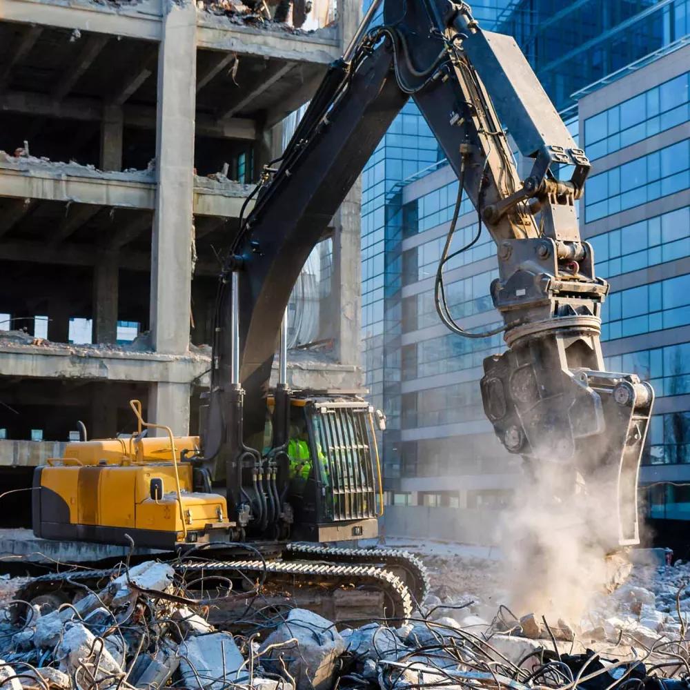 Excavator using a hydraulic demolition attachment to break reinforced concrete during commercial building demolition.