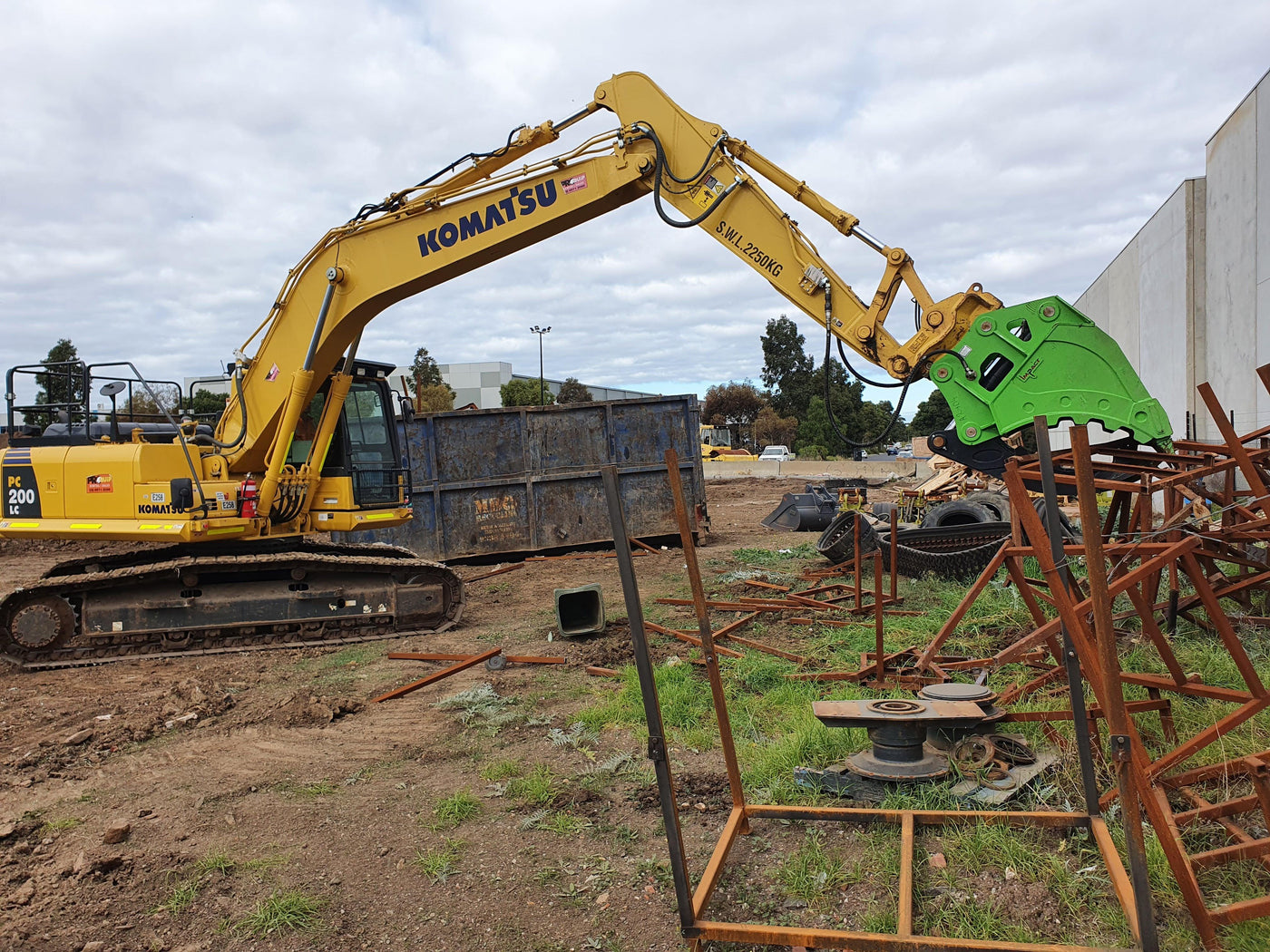 Excavator equipped with a hydraulic grapple attachment handling scrap metal on a construction and recycling site.