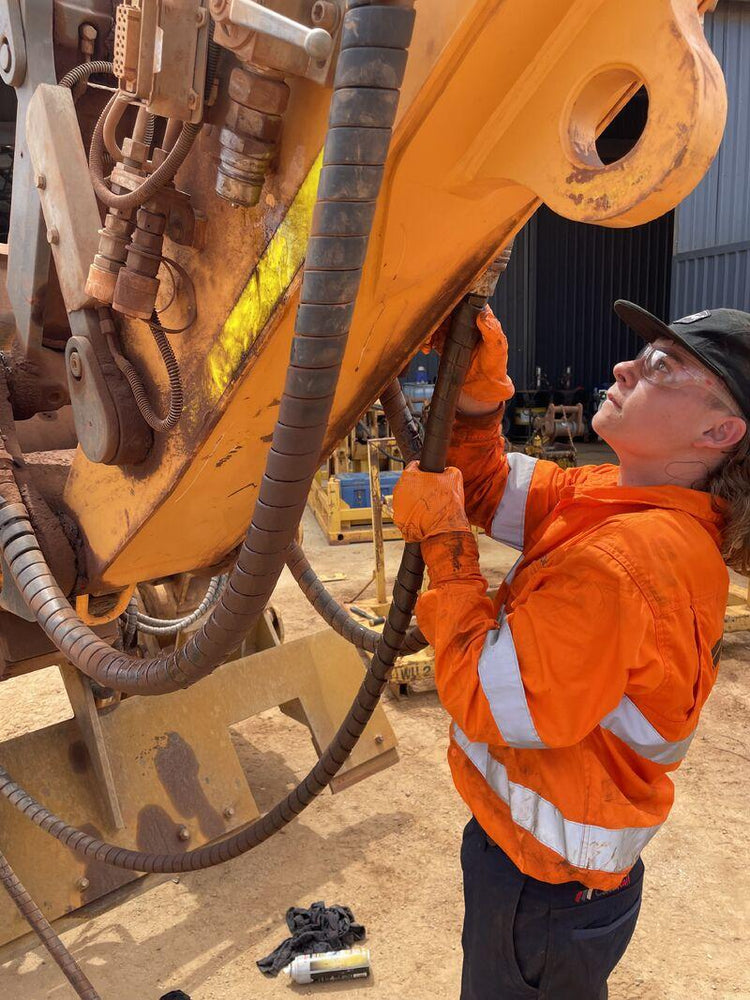 Excavator operator performing a pre-use safety inspection of an attachment and quick coupler before starting work.