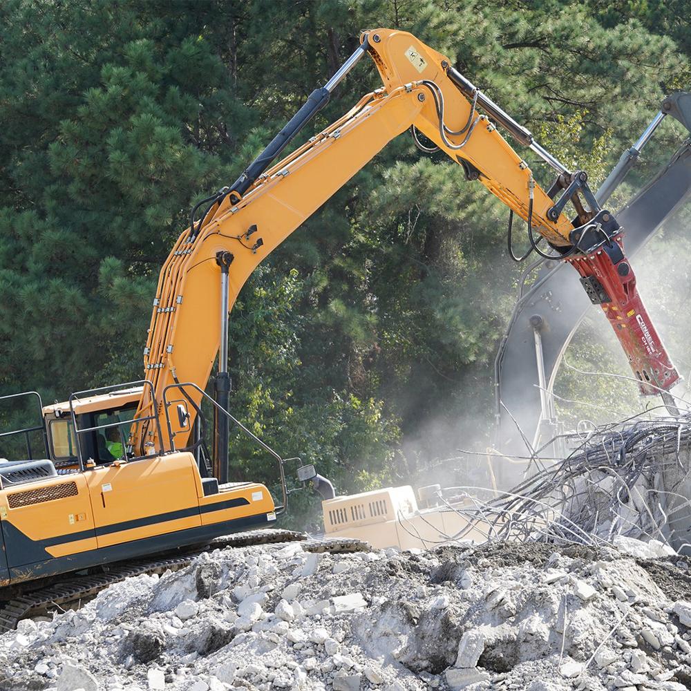 Excavator using a hydraulic breaker to demolish reinforced concrete with proper hydraulic flow and pressure.