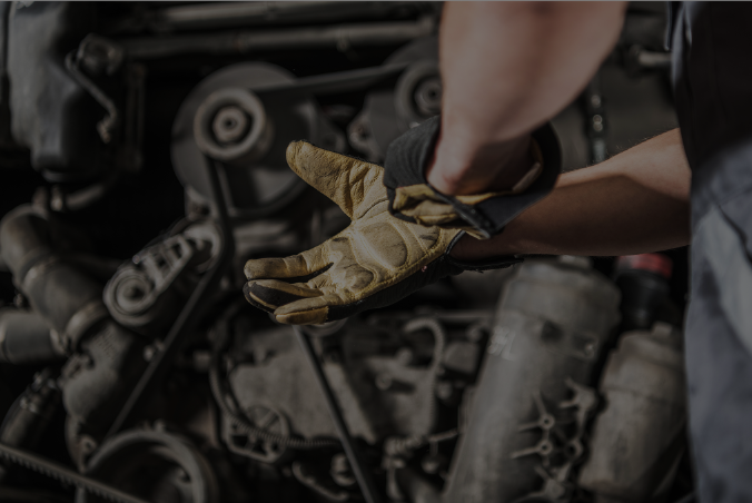 Mechanic's hand wearing a worn-out leather glove, with car engine parts in the background.