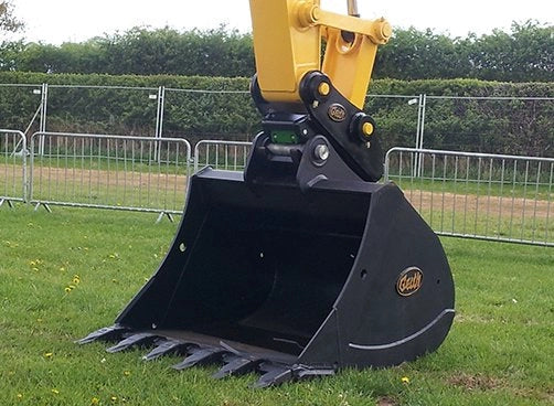 Geith Heavy Duty Bucket, showcasing its robust attachment to a yellow excavator arm, set against a green backdrop.