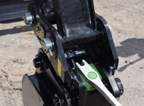Close-up of Geith Mechanical Quick Coupler's connectors and lever, displaying Geith logo, set against a gravel backdrop.