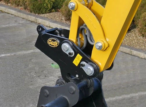 Close-up of Geith Hydraulic Quick Coupler attached to a machinery arm, showcasing its yellow and black color combination with visible safety labels.