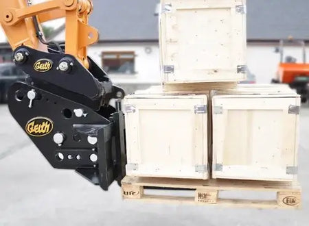 Geith universal pallet forks on an orange excavator, lifting wooden crates in a paved yard.